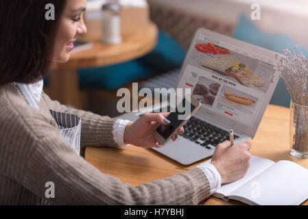Zufrieden lächelnde Frau, Notizen machen und mittels Handy. Stockfoto