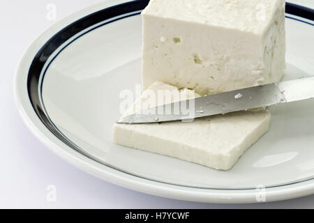 Scheibe Käse aus Kuhmilch und Messer in einem weißen Teller Stockfoto