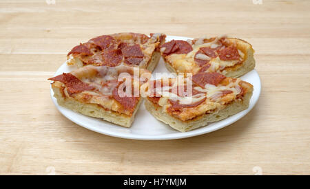 Einige Mikrowelle persönliche Größe Peperoni Pizza Scheiben isoliert auf einem weißen Teller oben auf einem Holztisch. Stockfoto