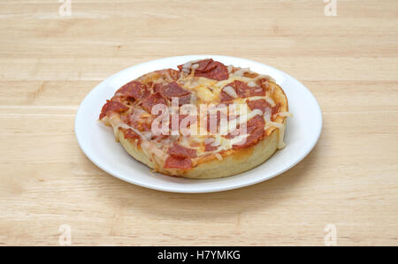Eine Mikrowelle persönliche Größe Peperoni-Pizza isoliert auf einem weißen Teller oben auf einem Holztisch. Stockfoto