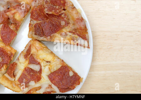 Enge Draufsicht von mehreren Mikrowelle persönliche Größe Peperoni Pizza Scheiben isoliert auf einem weißen Teller oben auf einem Holztisch. Stockfoto