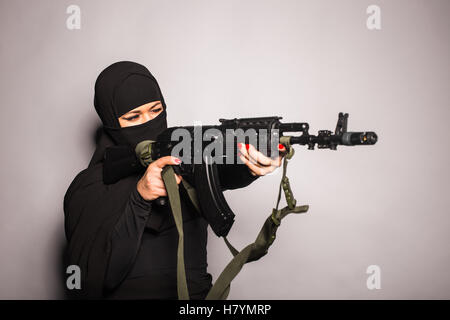 Muslimische Frau mit einem Maschinengewehr. Eine bewaffnete Frau schießt. Islamische Frau mit einer automatischen Waffe. Konzept von Krieg und Terrorismus Stockfoto