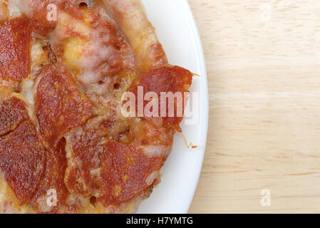 Enge Draufsicht eine Mikrowelle persönliche Größe Peperoni-Pizza isoliert auf einem weißen Teller oben auf einem Holztisch. Stockfoto