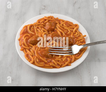 Eine Portion Spaghetti und Fleischbällchen mit einer Gabel auf einem weißen Teller oben auf einer grauen Marmor Tischplatte. Stockfoto
