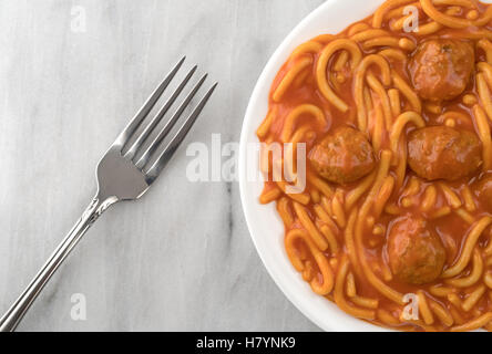 Draufsicht auf eine Portion Spaghetti und Fleischbällchen auf einem weißen Teller mit einer Gabel auf der Seite oben auf einer grauen Marmor Tischplatte. Stockfoto