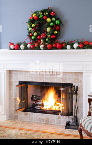 Weihnachten-Kamin mit bunten Dekorationen und und ein traditionelles Weihnachten Kranz oben ein loderndes Feuer im Kamin für eine warme co Stockfoto