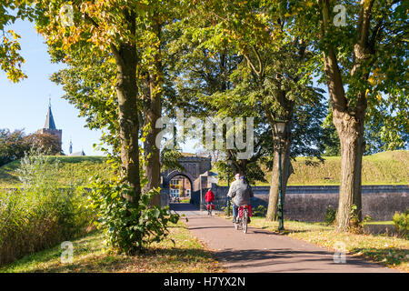 Menschen, die Reiten Fahrräder, Stadttor, Kirchturm und Wall der befestigten Stadt Naarden im Herbst, Niederlande Stockfoto