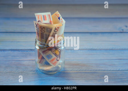 Transparentes Glas mit Geld drin. Textfreiraum. blauem Hintergrund Holz Stockfoto