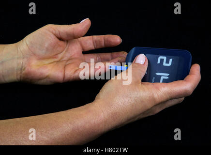 Eine Frau mit fortgeschrittenem Diabetes Blutzuckerspiegel mit einem Blutzuckermessgerät messen. Deutlich sichtbar ein Tropfen Blut auf einem Streifen Meas Stockfoto