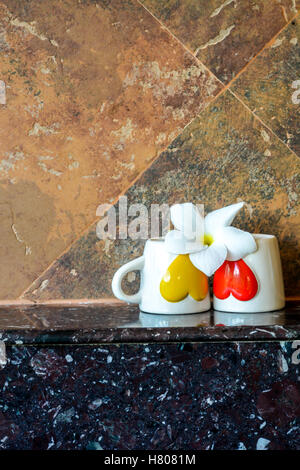 Zwei Kaffeetassen mit roten und gelben Herzen mit einer Blume auf Top, selektiven Fokus Stockfoto