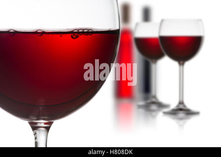 Gläser Rotwein mit Flaschen auf weißem Hintergrund Stockfoto