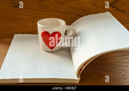 Weiße Tasse mit roten Herz auf weiße Buch auf Holztisch, selektiven Fokus auf Tasse mit Unschärfe Hintergrund Stockfoto