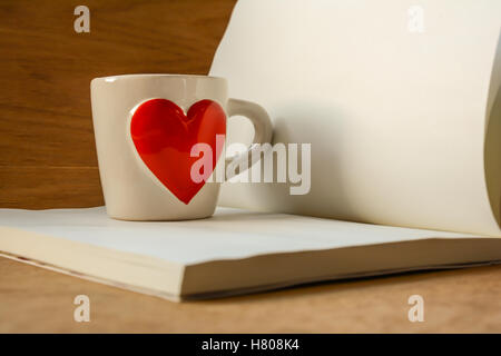 Valentinstag, Kaffeetasse mit roten Herzen und Notizblock für Ihren Text. Seitenansicht auf Holztisch, konzentrierte sich auf Tasse Stockfoto