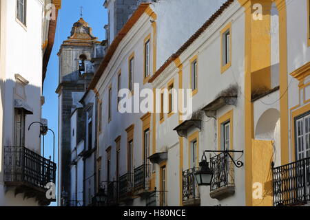 EVORA, PORTUGAL: typische schmale Straße mit Häusern lackiert in weiß und gelb und Santo Antao Kirche im Hintergrund Stockfoto