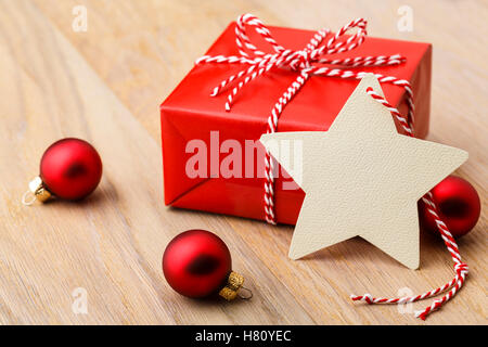 Einfache, klassische rote Weihnachtsgeschenk mit Ornamenten und handgemachte leer Geschenkanhänger auf rustikalen Holz horizontale Hintergrund vertreten. Stockfoto