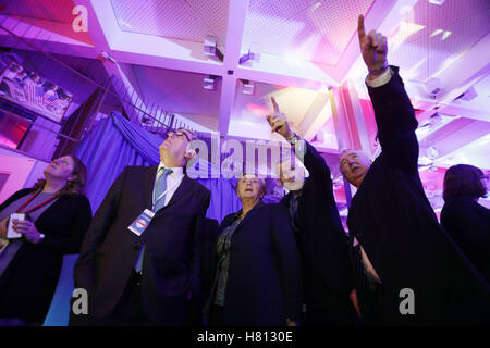 Die Gäste erreichen während der live-Feed auf einem großen Bildschirm auf der US-Präsidentschaftswahl Nacht Party in der US-Botschaft in London anschauen. Stockfoto