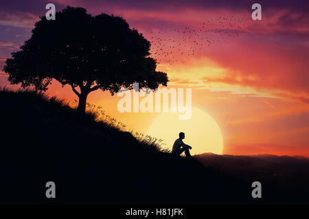 Junge sitzt alleine auf einem Hügel in der Mitte der Natur, über einen Sonnenuntergang Hintergrund. Abseits der Masse, die Heilung warten stehende Stockfoto