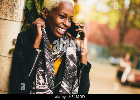 Moderne junge afroamerikanische Frau hält mobile Hone lächelnd im Herbst im freien Stockfoto