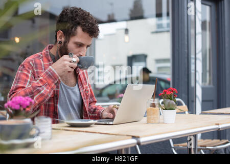 Junge tätowierte Hipster mit Laptop vor café Stockfoto