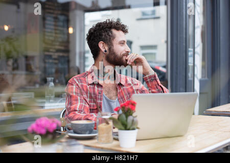Junge tätowierte Hipster mit Laptop vor café Stockfoto