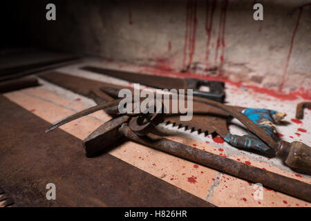 Nahaufnahme von Sägen, Sicheln, Hammer und andere Geräte auf dem blutigen Boden im Keller in einem Halloween-Horror-Konzept Stockfoto