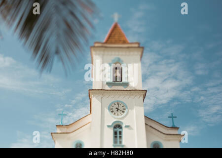 Kippen Sie richtig Shift Foto einer gewöhnlichen Kirche mit Glockenturm und Uhr in Rio De Janeiro, Palmzweig vor und blauer Himmel Stockfoto