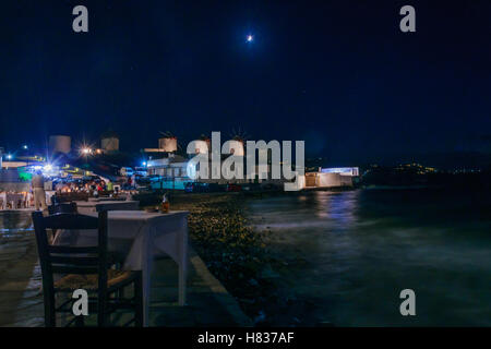 MYKONOS, Griechenland - 2. Oktober 2011: Nachtszene von Dorf und Strand mit lokalen Unternehmen, Windmühlen, einheimische und Besucher, Stockfoto