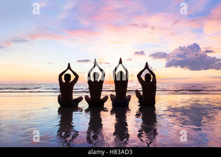 Gruppe von vier Personen üben Meditation und Yoga am Strand bei Sonnenuntergang - Konzept über Freunde, Familie, Harmonie und gesund Stockfoto