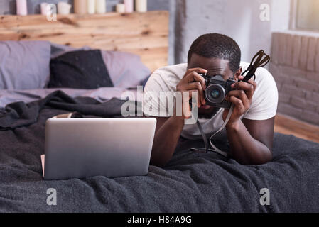 Junger Mann hält eine Kamera in seinem Schlafzimmer Stockfoto