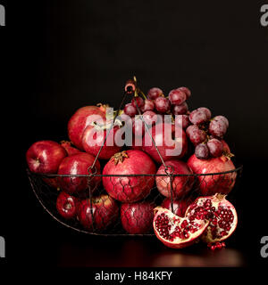 Still-Leben auf einem dunklen Hintergrund. Früchte und Beeren (Äpfel, Granatäpfel und Trauben) in den Korb. Stockfoto