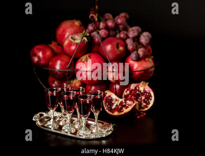 Still-Leben auf einem dunklen Hintergrund. Weingläser (Liquor), Früchte und Beeren (Äpfel, Granatäpfel und Trauben) in den Korb. Stockfoto