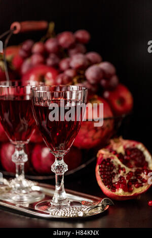 Still-Leben auf einem dunklen Hintergrund. Weingläser (Liquor), Früchte und Beeren (Äpfel, Granatäpfel und Trauben) in den Korb. Stockfoto