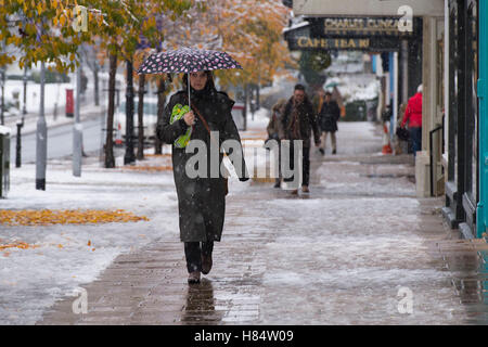 Ilkley, West Yorkshire, Großbritannien. 9. November 2016. Es schneit und Fußgänger (tragen Stiefel, Wintermäntel und halten Regenschirme) sind Fuß vorbei an Geschäften auf The Grove - Ilkleys ersten Schneefall 2016. Bildnachweis: Ian Lamond/Alamy Live-Nachrichten Stockfoto