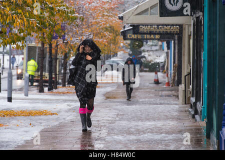 Ilkley, West Yorkshire, Großbritannien. November 2016. Es schneit und Fußgänger (mit wellington-stiefeln, Schals und Wintermänteln mit Hauben oben) laufen an Geschäften auf dem Grove vorbei. Im Vordergrund steht eine junge Frau (Kapuze über Kopf, Schal, Schweißen). Ilkleys erster Schneefall 2016. Credit: Ian Lamond/Alamy Live News Stockfoto