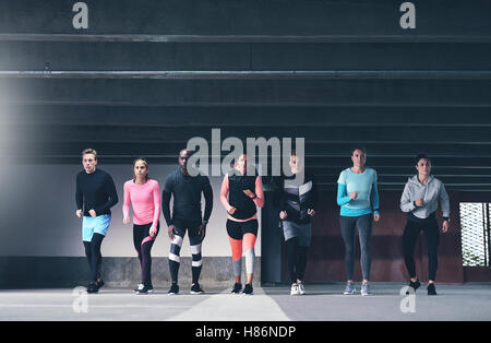 Gruppe der multiethnischen jungen Athleten, die Vorbereitung auf ein Rennen durch eine geräumige kommerzielle Tiefgarage Schlange vor t Stockfoto