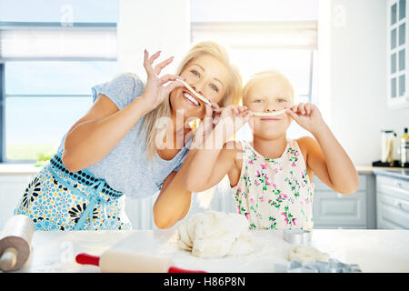Spielerische Mama und Tochter mit Gebäck Schnurrbärte Backen zusammen in der Küche und bereitet einen Hügel aus Teig, high-Key Hintergrund wi Stockfoto