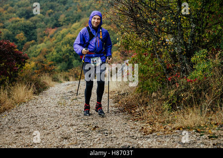 junger Mann mit walking-Stöcken laufen bei Regenwetter auf Bergweg während Crimea Bergmarathon Stockfoto