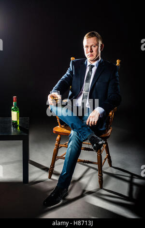 Der glückliche Geschäftsmann Glas Whisky und Blicke in die Kamera hält. Studio gedreht. Stockfoto