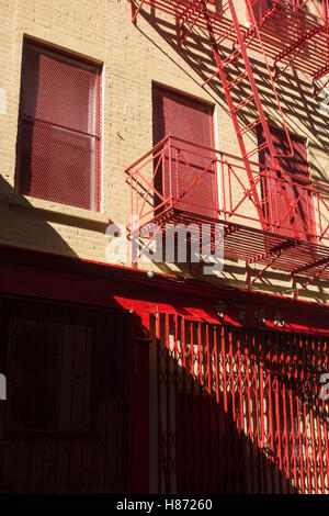 Eine bunt bemalte rote Feuerleiter ein Tor auf einen alten gelben Mietshaus in New York City Stockfoto