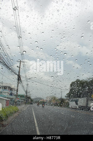 Regentropfen auf dem Autoglas mit Straße Hintergrund und Wolken am Himmel Stockfoto