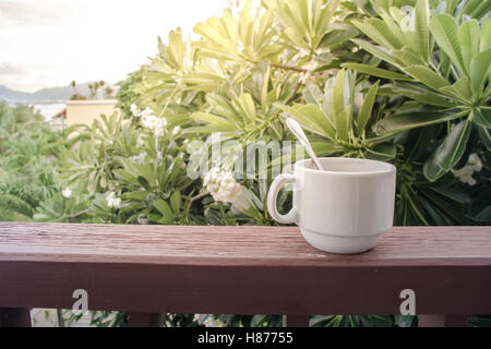 Kaffeetasse mit Kaffeelöffel auf dem hölzernen Balkon mit Sonnenlicht in den Morgen und Natur Hintergrund Stockfoto