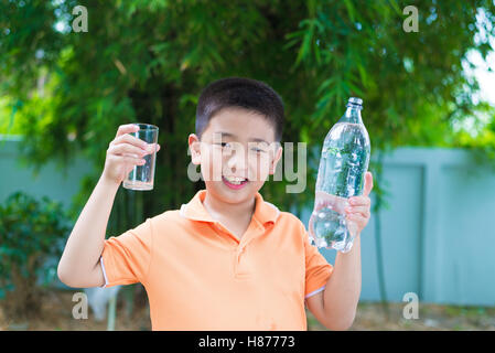 Asiatische junge gießt Wasser in Glas aus Flasche, im Garten, grüner Hintergrund Stockfoto