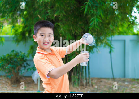 Asiatische junge gießt Wasser in Glas aus Flasche, im Garten, grüner Hintergrund Stockfoto