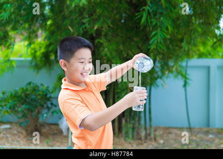 Asiatische junge gießt Wasser in Glas aus Flasche, im Garten, grüner Hintergrund Stockfoto