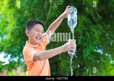 Asiatische junge gießt Wasser in Glas aus Flasche, im Garten, grüner Hintergrund Stockfoto