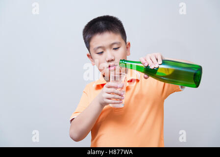 Asiatische junge gießt Wasser in Glas aus einer grünen Flasche auf graue Wand Hintergrund mit weichen Schatten Stockfoto