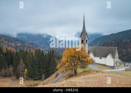 Nebligen Herbstmorgen in der San Lorenzo Kirche in Sauris di Sopra, Dolomiten, Italien. Stockfoto