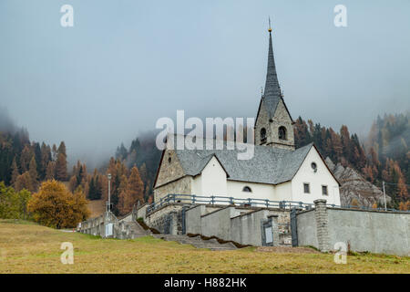 Nebligen Herbstmorgen in der San Lorenzo Kirche in Sauris di Sopra, Dolomiten, Italien. Stockfoto