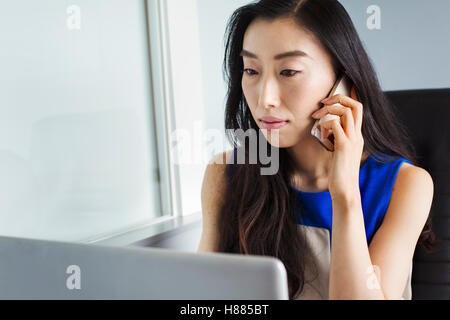 Eine Geschäftsfrau Vorbereitung auf Arbeit, sitzen mit ihrem Laptop und sprechen auf ihr Smartphone. Stockfoto