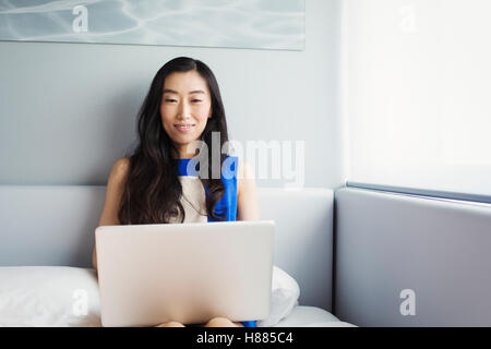 Eine Geschäftsfrau, die Vorbereitung für die Arbeit, sitzt auf einem Bett mit ihrem Laptop-Computer. Stockfoto